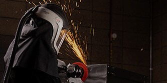 Trabajador con máscara desbastando metal con un disco para la preparación de superficies de uso intensivo Scotch-Brite™ Precision
