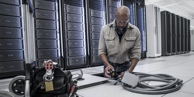 trabajador en un centro de datos instalando conductos eléctricos bajo el suelo
