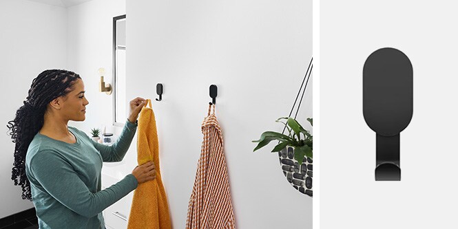 Mujer colgando toallas en ganchos de pared negros 3M CLAW™ en el baño
