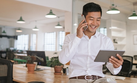 Imagen de un hombre de negocios sonriente que habla por teléfono y mira una tableta.
