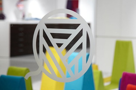 Ventana de vidrio transparente con un logotipo con aspecto de vidrio grabado y formas de colores detrás.
