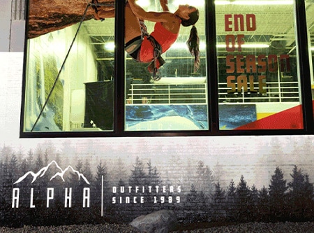 Exterior de tienda minorista de noche, con lámina para gráficos impresa para ventanas y lámina retroreflectante impresa con un motivo de árboles y logotipo.
