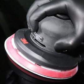 Primer plano de guante negro con una lijadora rotorbital eléctrica y neumática 3M™ 