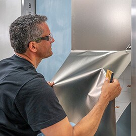 Hombre instalando un acabado metálico plateado 3M DINOC en la puerta de un ascensor