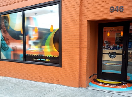 Exterior de edificio de ladrillo naranja con láminas para gráficos en las ventanas y la acera.
