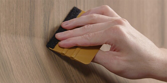 Primer plano de la escobilla de goma que se utiliza para instalar una lámina con un patrón de madera
