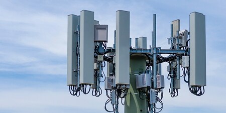 Parte superior de una torre de antena contra un cielo azul.
