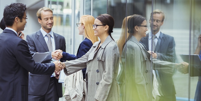 Grupo de empresarios saludándose frente a un edificio de oficinas cubierto de ventanas
