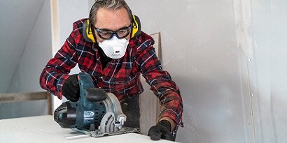 Hombre con mascarilla respiratoria y orejeras auriculares sierra madera
