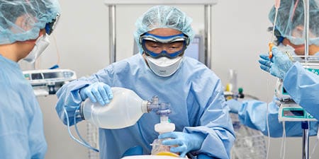 Imagen que muestra a 3 trabajadores sanitarios usando EPI mientras atienden a un paciente
