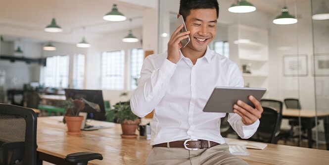 Imagen de un hombre de negocios sonriente que habla por teléfono y mira una tableta.
