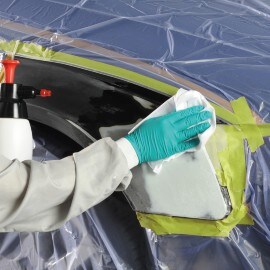 Una mano con un guante verde desengrasando una parte de una carrocería con una toallita blanca