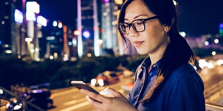 Mujer utilizando su dispositivo móvil en una ciudad de noche.
