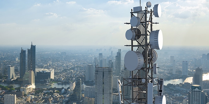 Una gran antena instalada con el horizonte de una ciudad de fondo.
