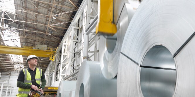 Trabajador moviendo rollos de planchas metálicas
