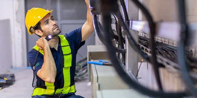 Trabajador con equipo de seguridad revisando conexiones eléctricas con una linterna
