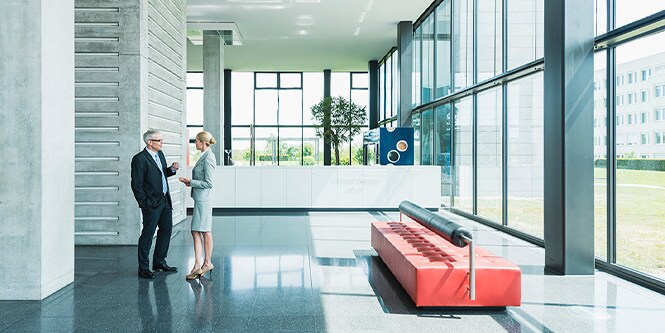 Panorámica del vestíbulo de un edificio de oficinas moderno con paredes de ventanas y dos empresarios charlando
